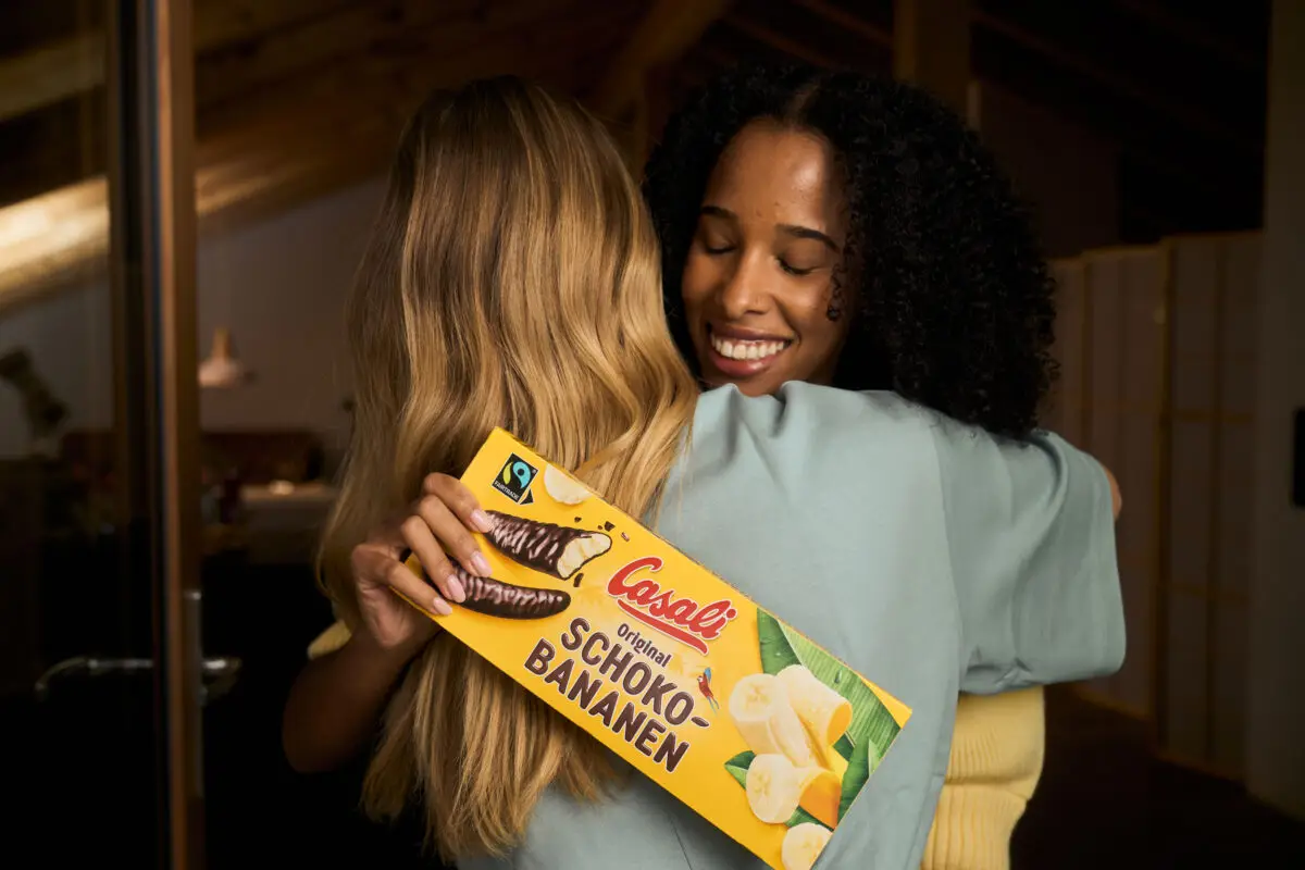 Zwei Frauen umarmen sich mit einer Packung Schoko-Bananen