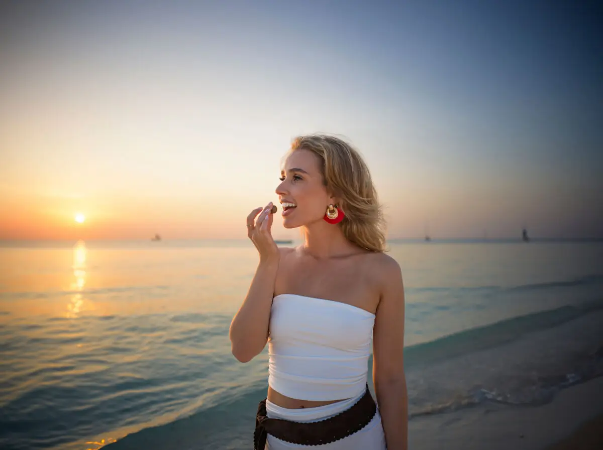 Eine blonde Frau isst eine Rum-Kokos Kugel am Strand