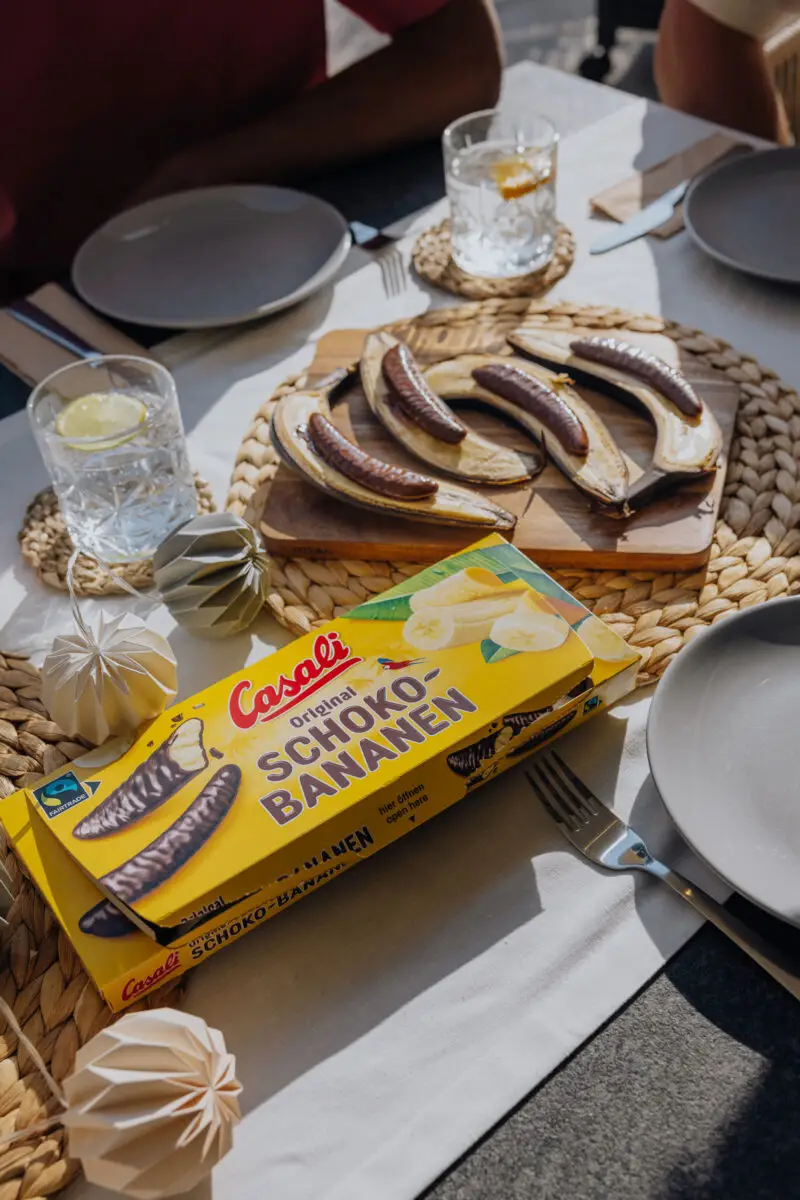 Eine Packung Schoko-Bananen auf gedecktem Tisch mit Bananenhälften mit Schoko-Bananen