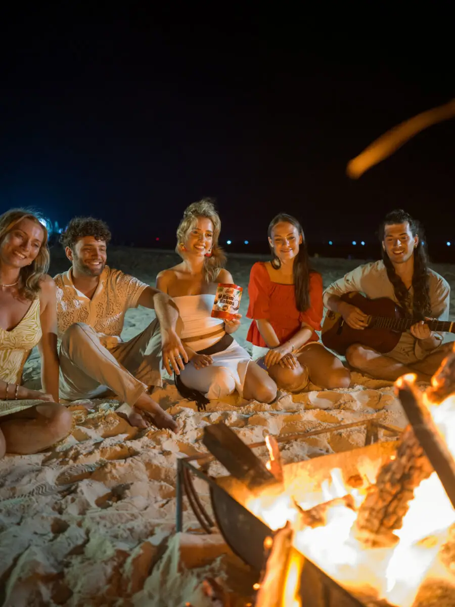 Junge Menschen teilen sich eine Packung Casali Rum-Kokos Kugeln am Strand beim Lagerfeuer